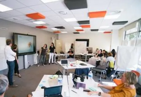 Plusieurs individus réunis autour de tables dans une pièce, engagés dans des conversations animées.
