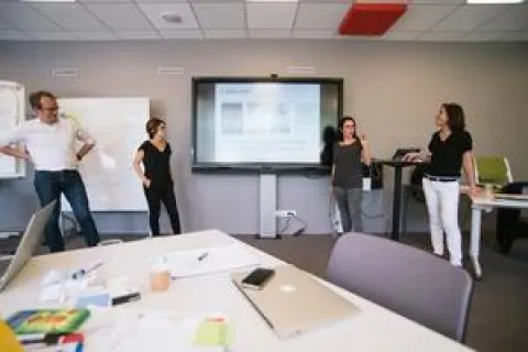 Un groupe de personnes dans un bureau, devant un écran de projecteur, discutant et collaborant sur un projet.