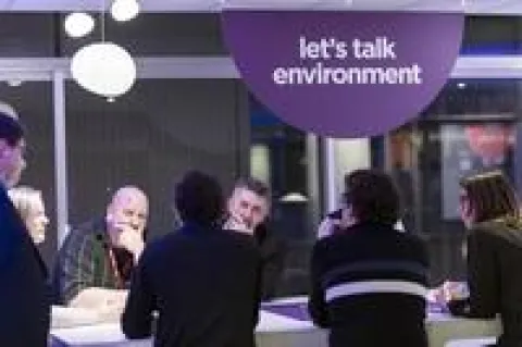 Une équipe travaille avec une PME Des personnes assises à des tables dans une salle avec une pancarte indiquant "Discutons de l'environnement".